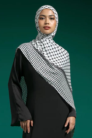 Woman wearing a black outfit with a white and black checkered hijab by Lozy Hijab against a green background