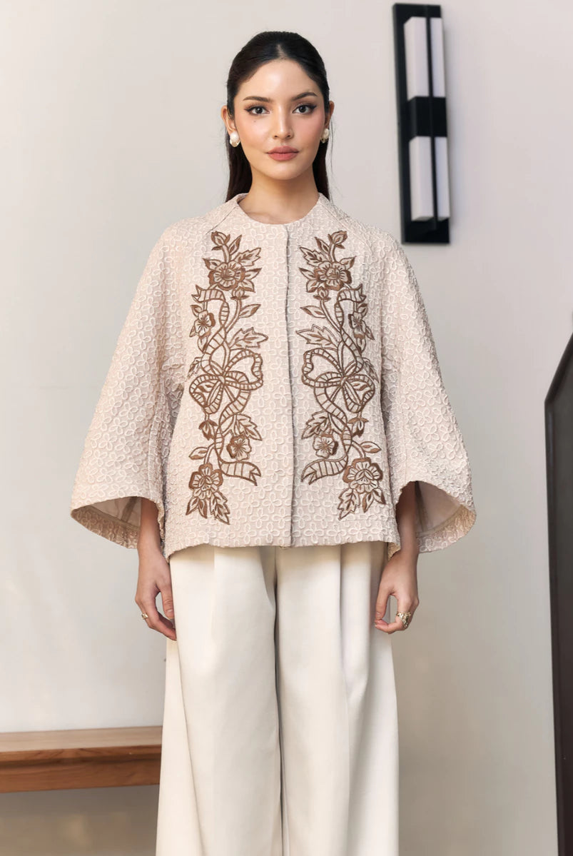Woman wearing a beige embroidered outer by Studio Tui in an indoor setting.