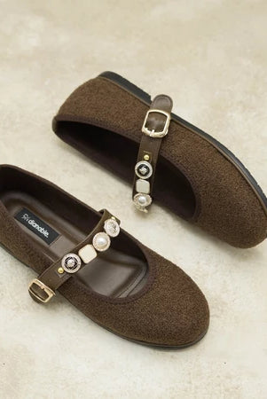 Dark brown flat shoes by Dianable with decorative straps on a textured surface