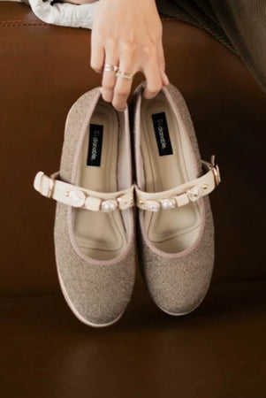 Pair of beige flat shoes with a decorative strap by Dianable on a brown surface