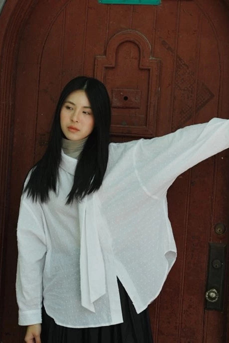 Woman in a white shirt by Yestoday standing in front of a wooden door