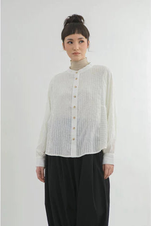 Person wearing a light-colored button-up shirt by Yestoday and dark pants on a white background