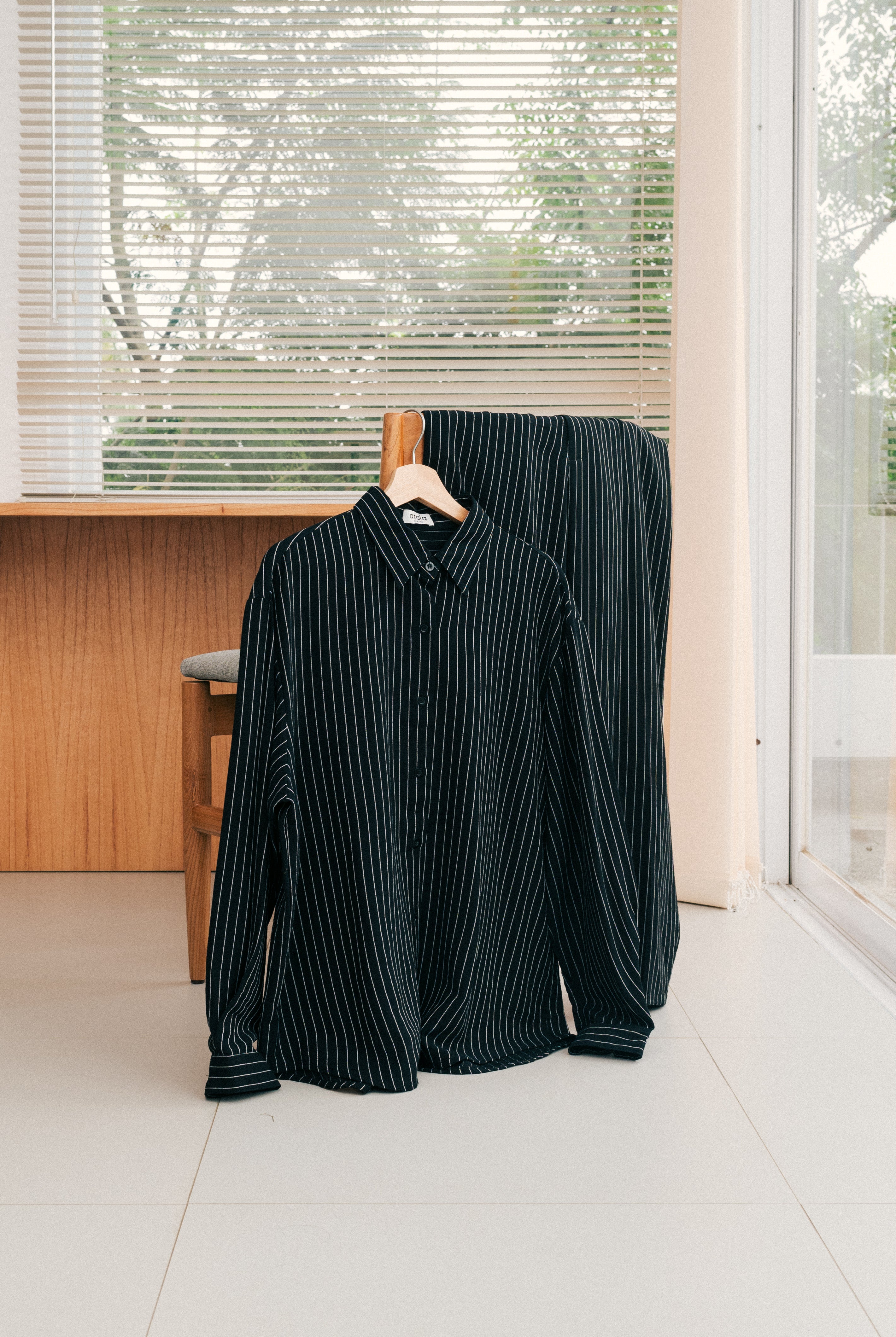 Black striped shirt and pants from Atala Scarves on a hanger in a room with large windows.