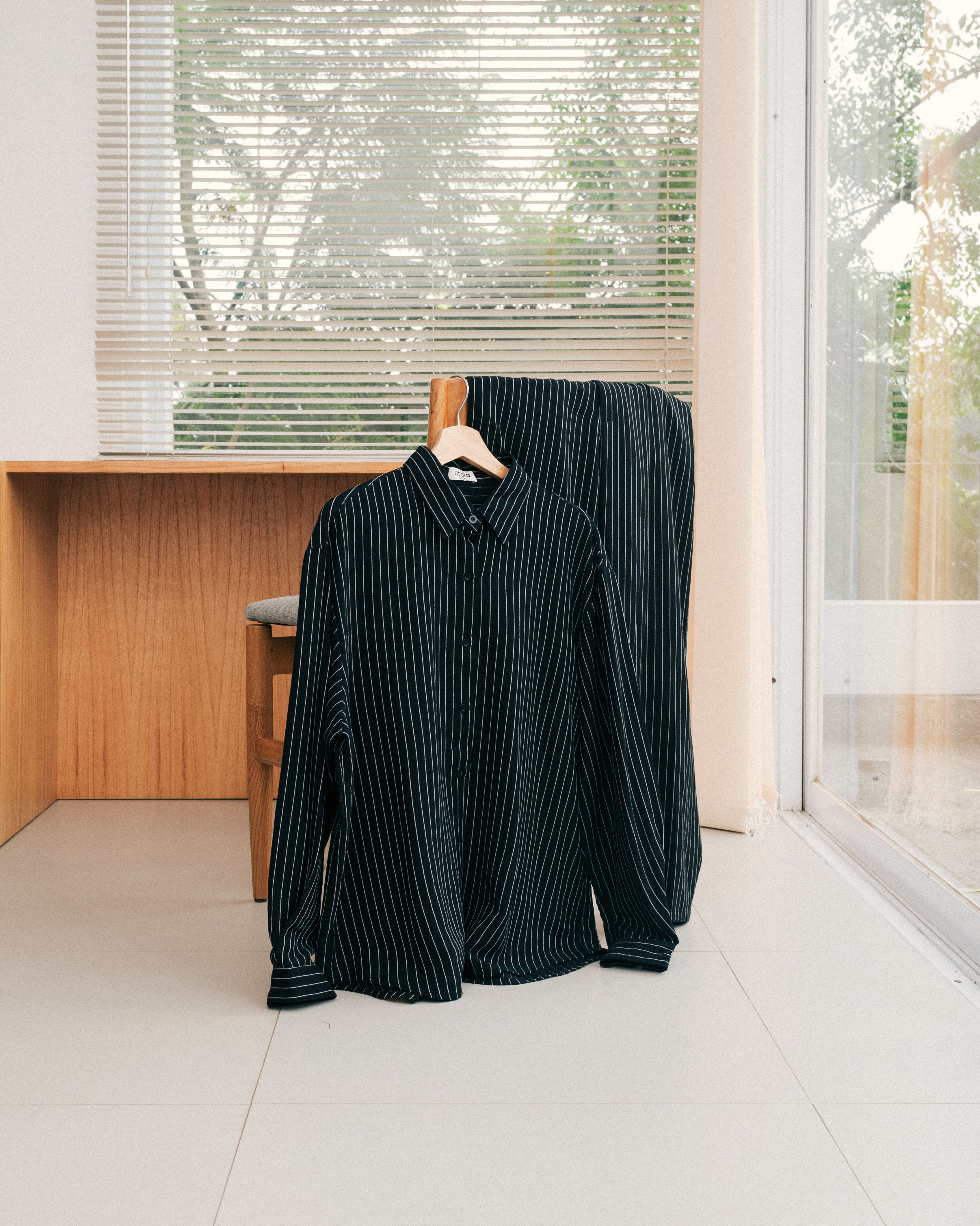 Black striped shirt and pants from Atala Scarves on a hanger in a room with large windows.