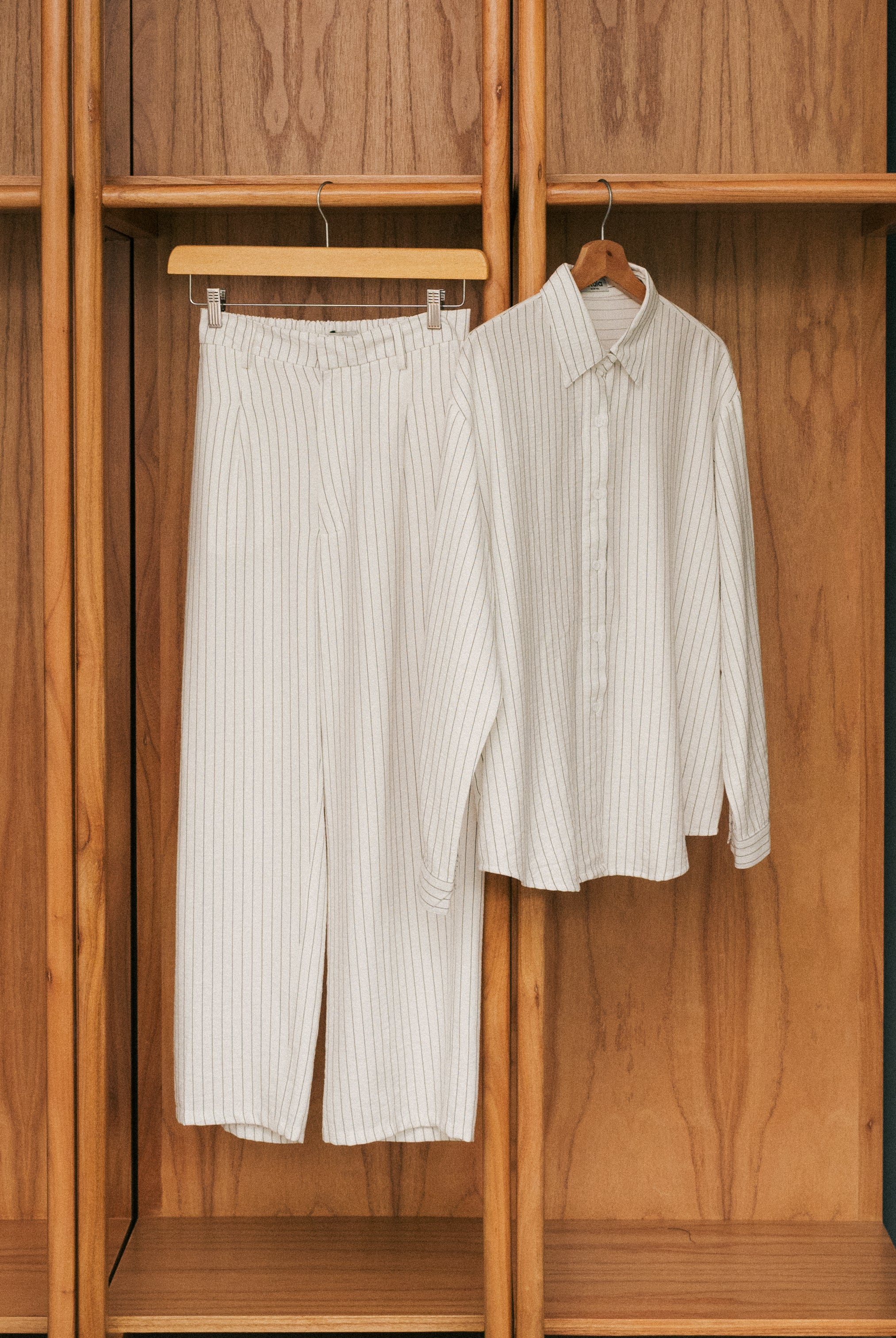 Broken white striped shirt and pants from Atala Scarves hanging on a wooden wardrobe.