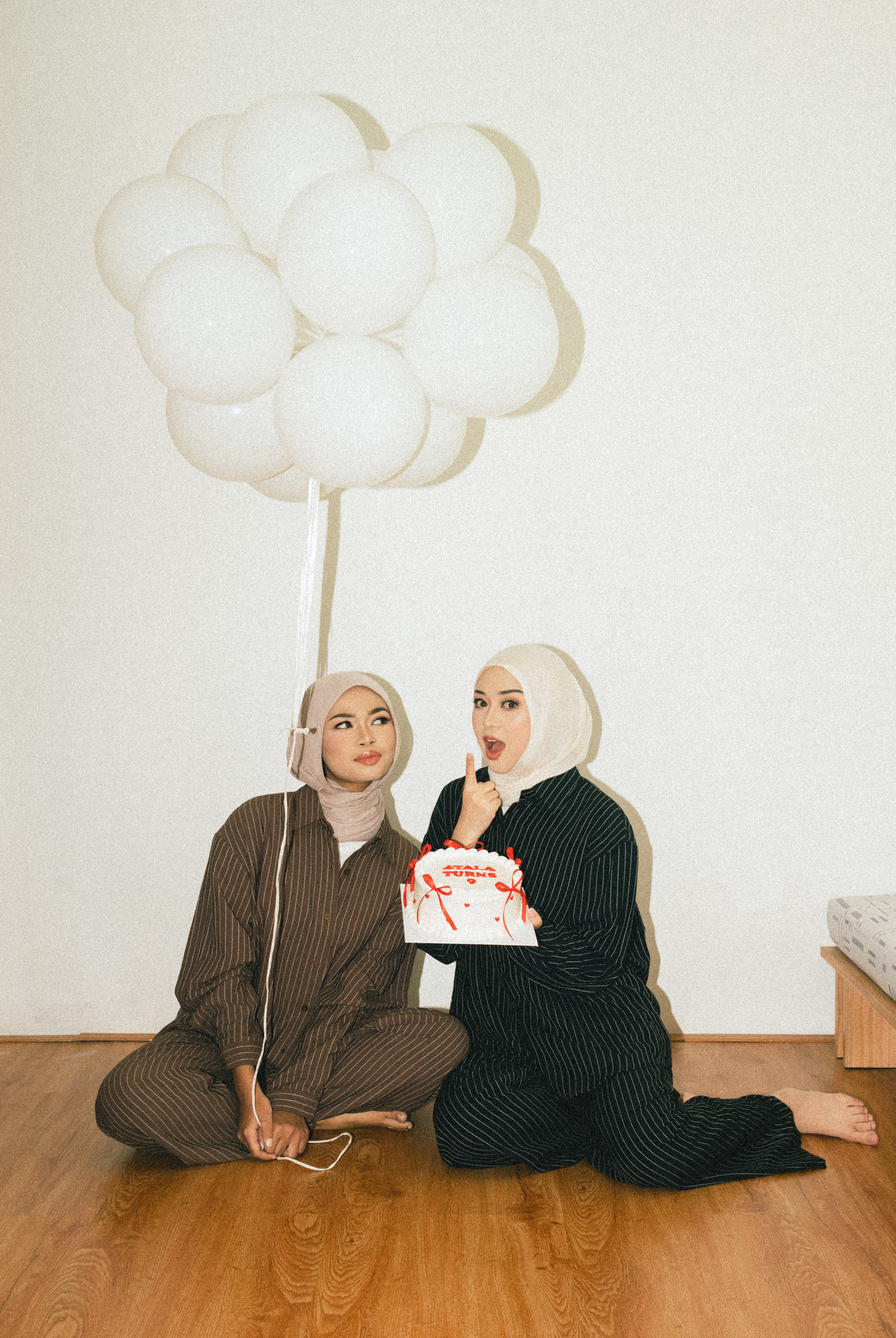 Two people sitting on the floor with balloons and a box, wearing linen outfit from Atala Scarves.
