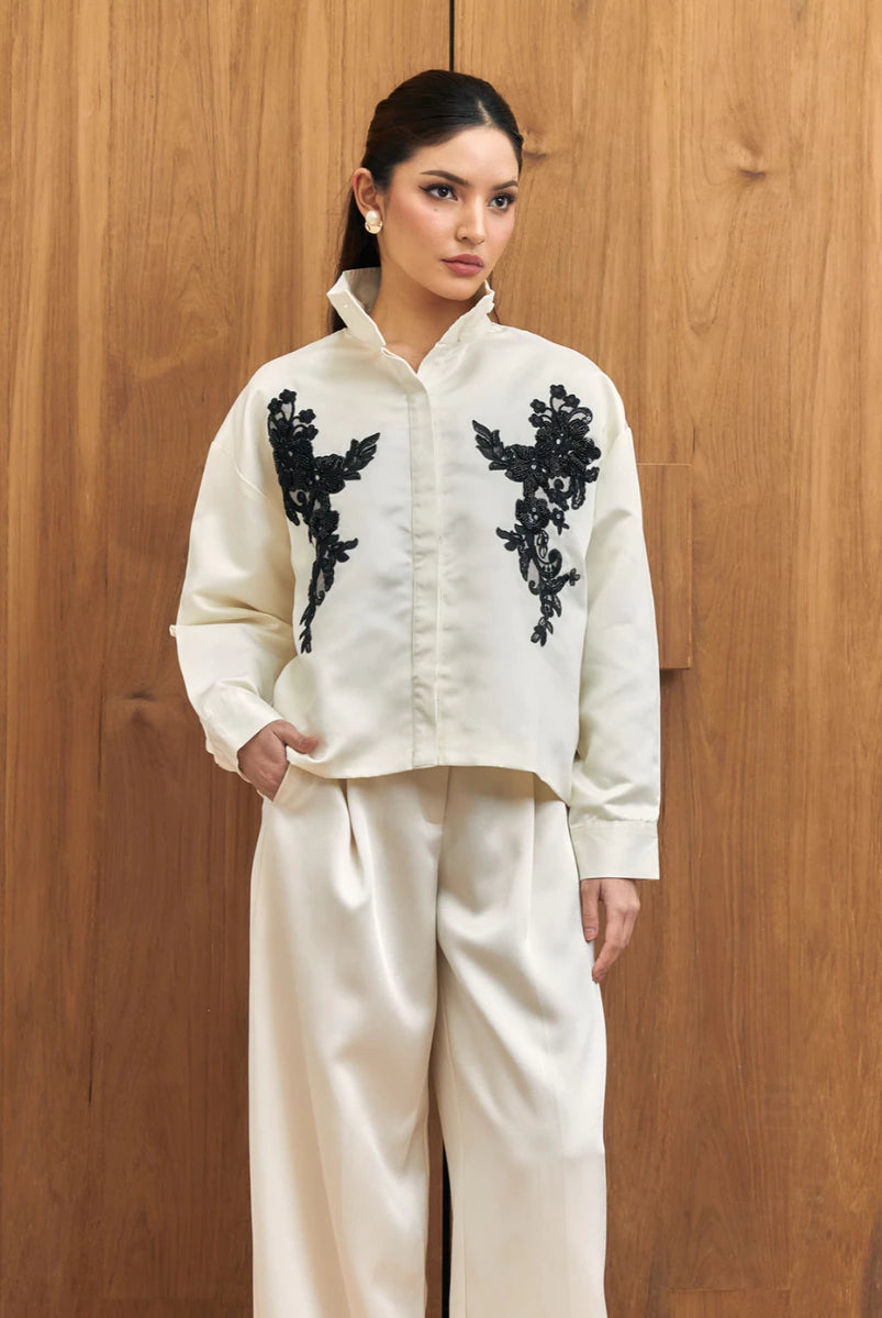Woman wearing a white shirt with black floral embroidery by Studio Tui against a wooden background