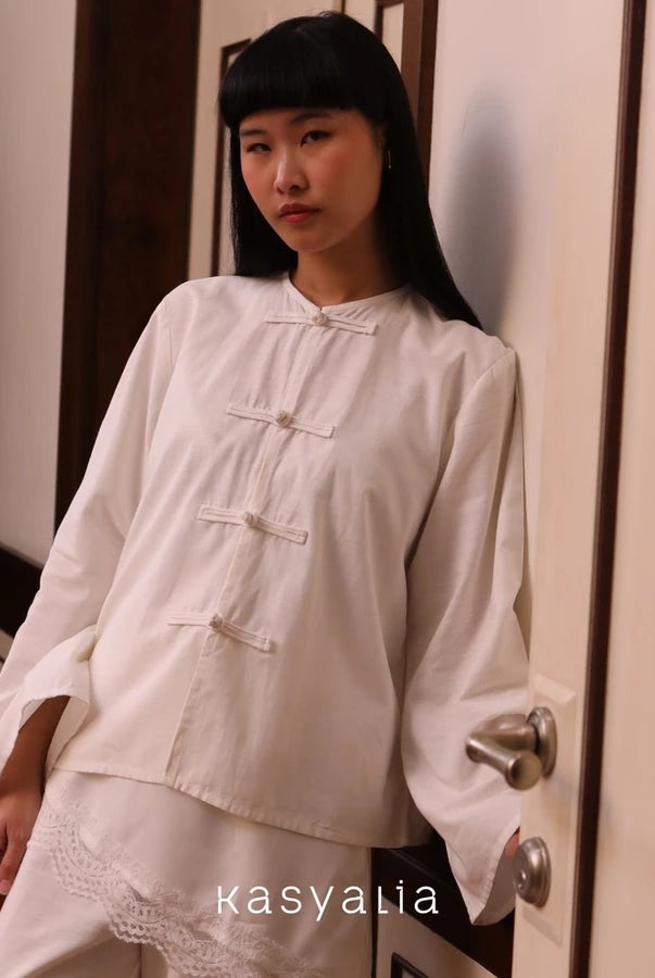 Woman wearing a white blouse by Kasyalia standing in a room with a door.