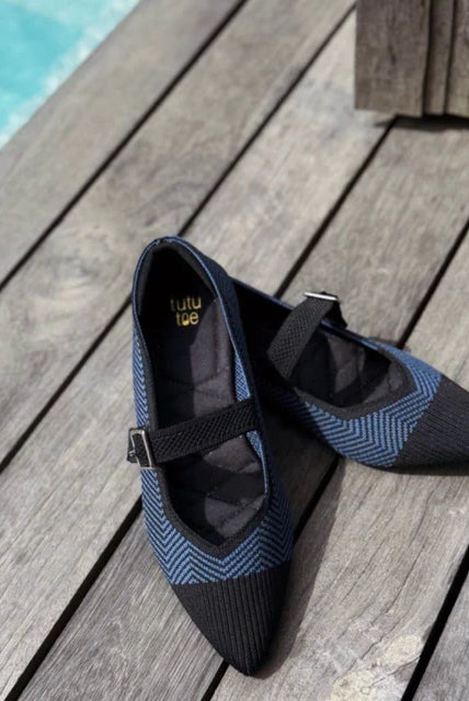 Pair of black and blue flatshoes by Tutu Toe on a wooden deck near a pool.