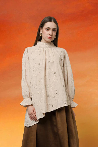 Woman wearing a light beige blouse with floral patterns by Kasa Heritage and brown pants against an orange gradient background