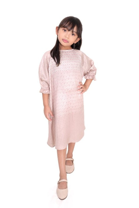 A girl in a pink midi-length tunic with long sleeves, standing against a plain background.