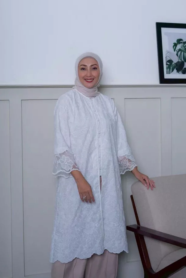 Woman wearing a white lace tunic by Abame standing in a room with a white wall and a framed picture.
Seorang wanita mengenakan tunik renda putih dari Abame berdiri di dalam ruangan dengan dinding putih dan sebuah foto dalam bingkai.