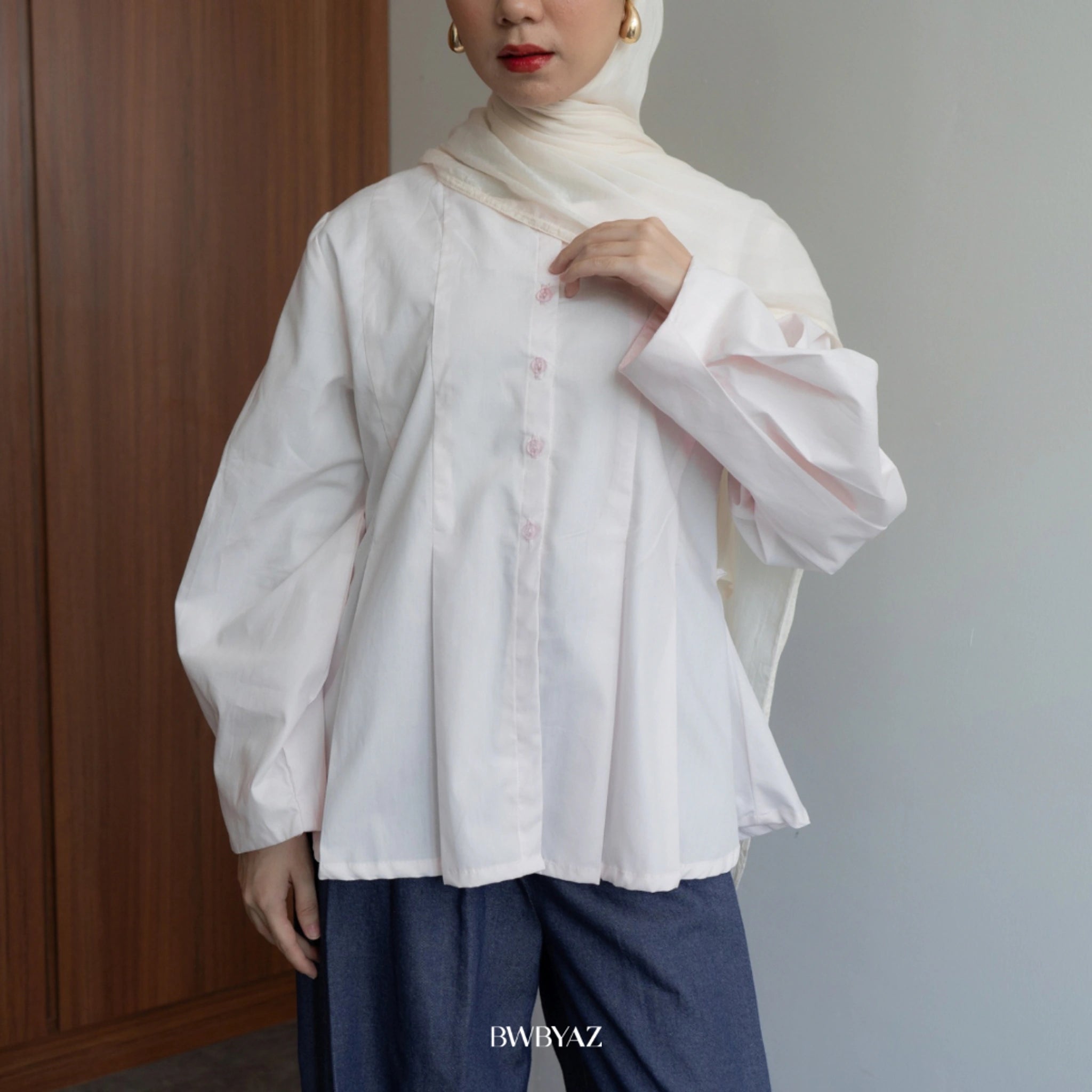 A person wearing a long sleeve soft pink peplum blouse with a round neckline from BWBYAZ and a denim skirt.