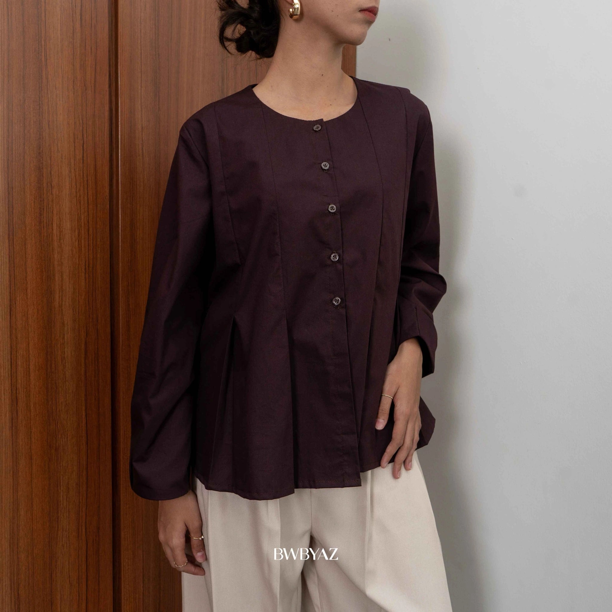 A person wearing a long sleeve dark brown peplum blouse with a round neckline from BWBYAZ and a denim skirt.