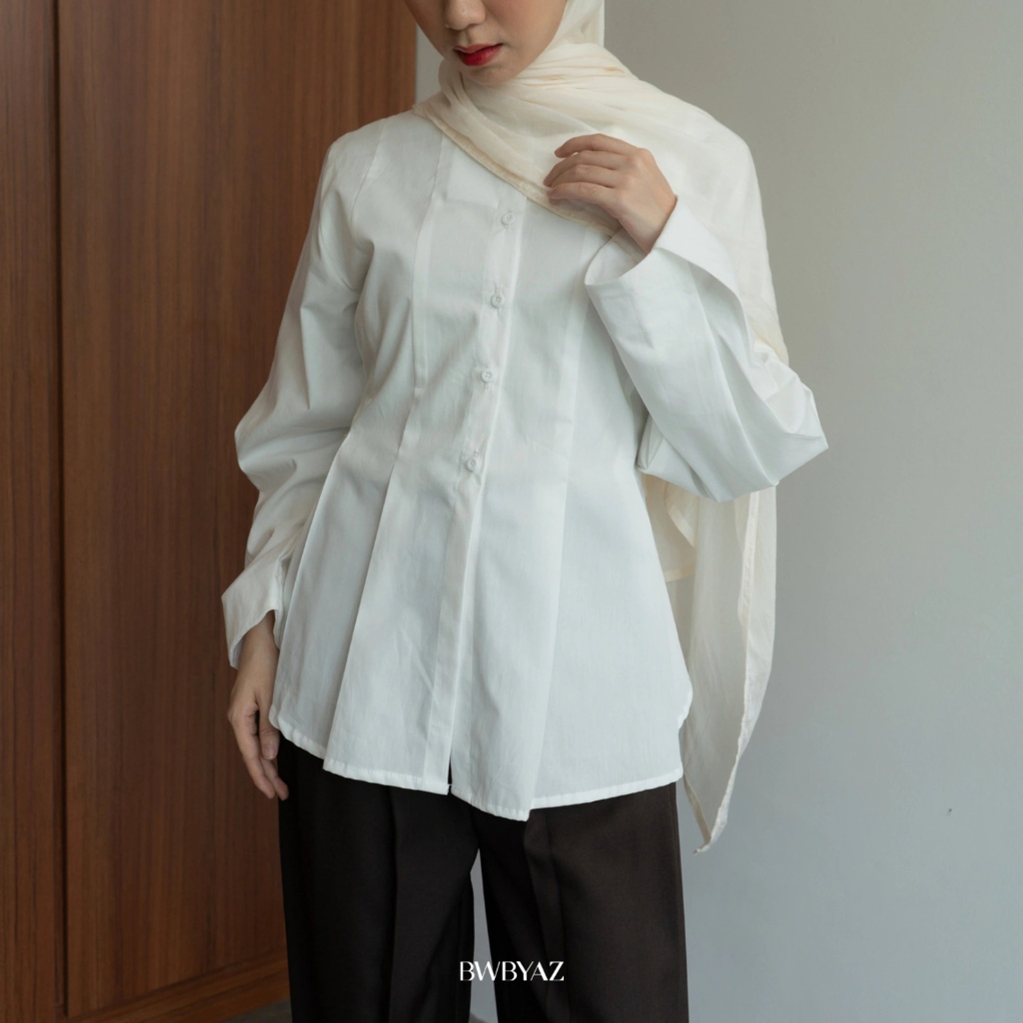 Person wearing a long sleeves white peplum blouse from BWBYAZ and hijab against a neutral background