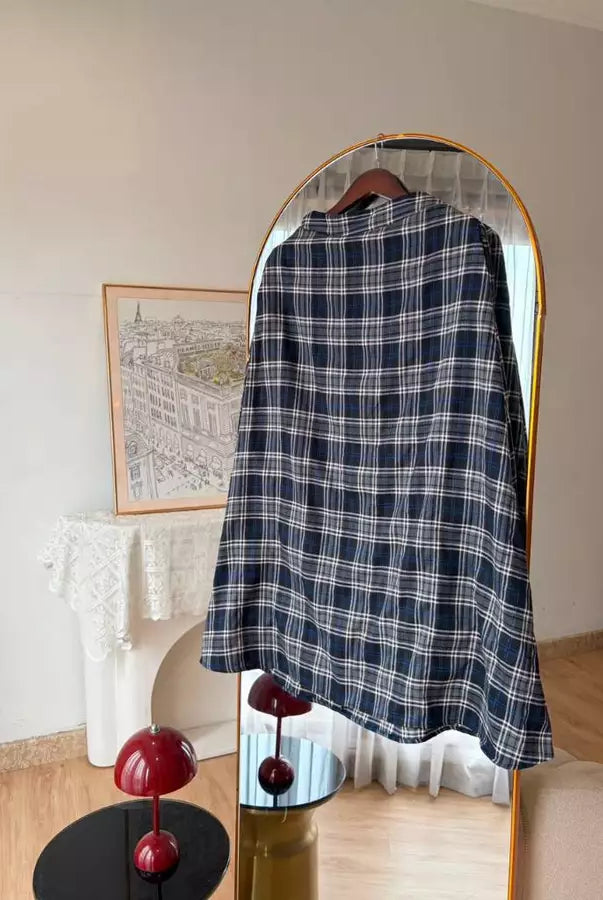 A navy blue and white plaid shirt by Haidee Orlin hanging on a wooden hanger in front of a gold-framed arched mirror, set in a styled room with a fireplace and decorative red mushroom lamps.