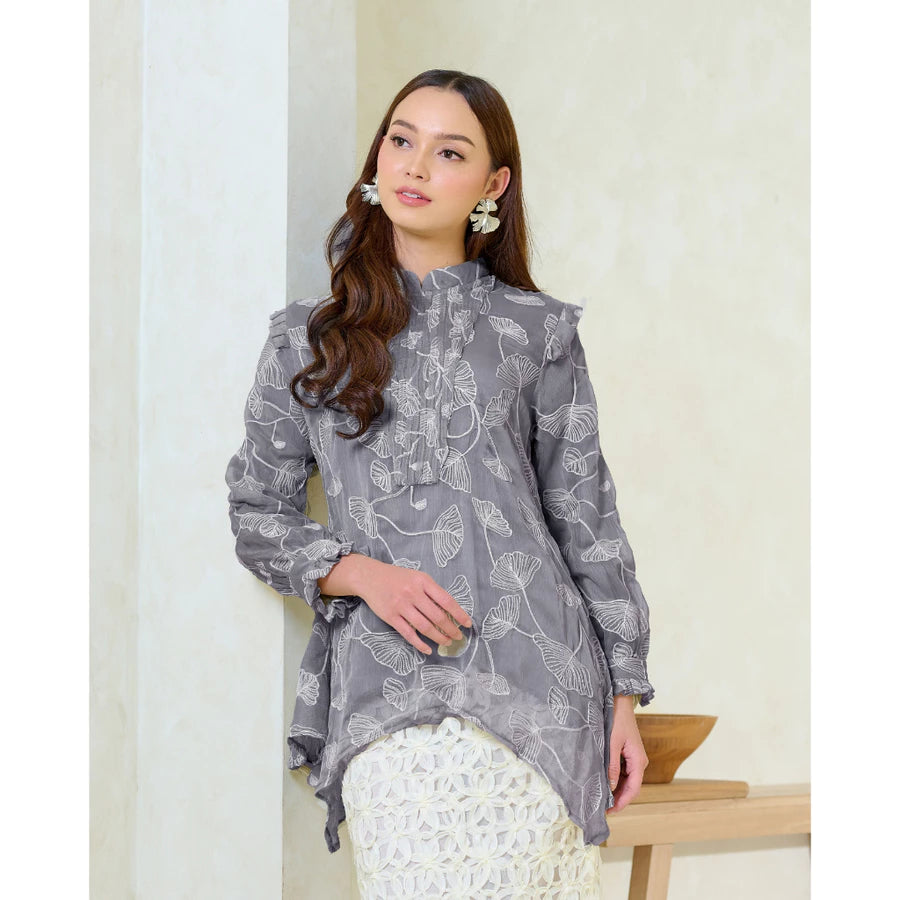 Woman wearing a gray patterned blouse by Kasa Heritage with a white skirt against a light background