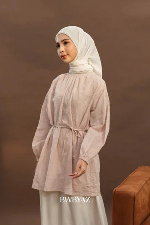 A woman wearing a long pink floral tunic with tie details at the neckline and bishop sleeves with elastic cuffs from BWBYAZ.