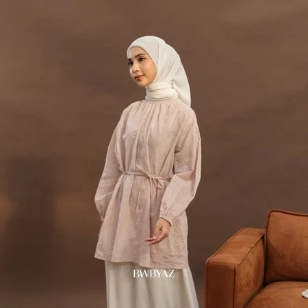 A woman wearing a long pink floral tunic with tie details at the neckline and bishop sleeves with elastic cuffs from BWBYAZ.