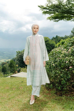 Woman in a light green outfit set of tunic and pants from Haidee Orlin standing in a scenic outdoor setting with trees and grass.