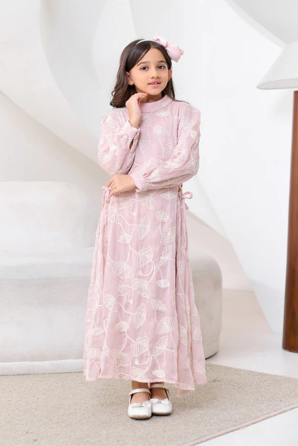 Young girl in a pink floral dress by Kasa Heritage standing in a room with a white wall and wooden lamp.