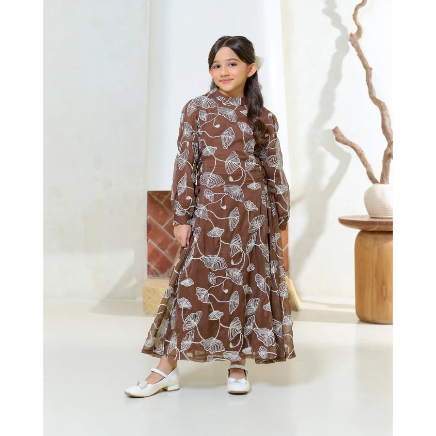 Young girl wearing a brown dress by Kasa Heritage with white floral patterns in a minimalistic room.