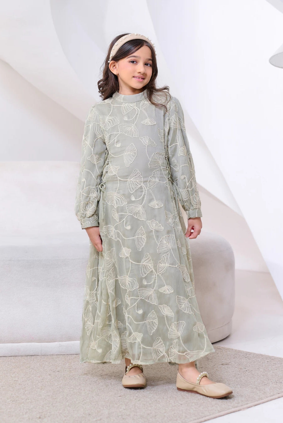 Young girl wearing a light green dress by Kasa Heritage with floral patterns on a white background