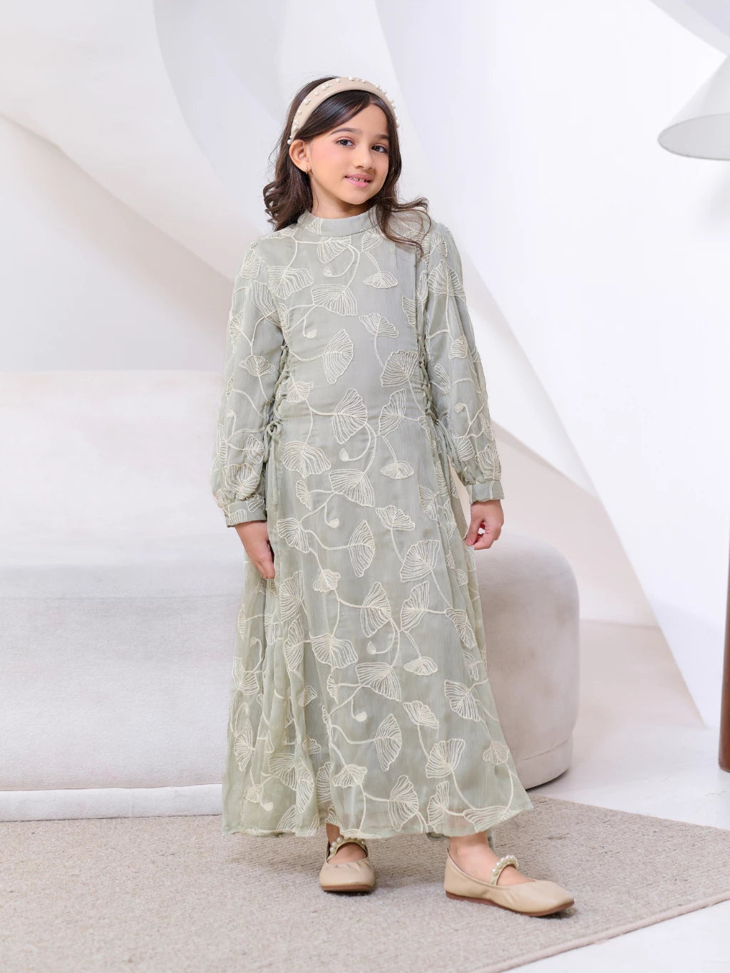 Young girl wearing a light green dress by Kasa Heritage with floral patterns on a white background