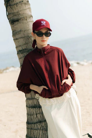 Person wearing a maroon track jacket by Haidee Orlin and cap.