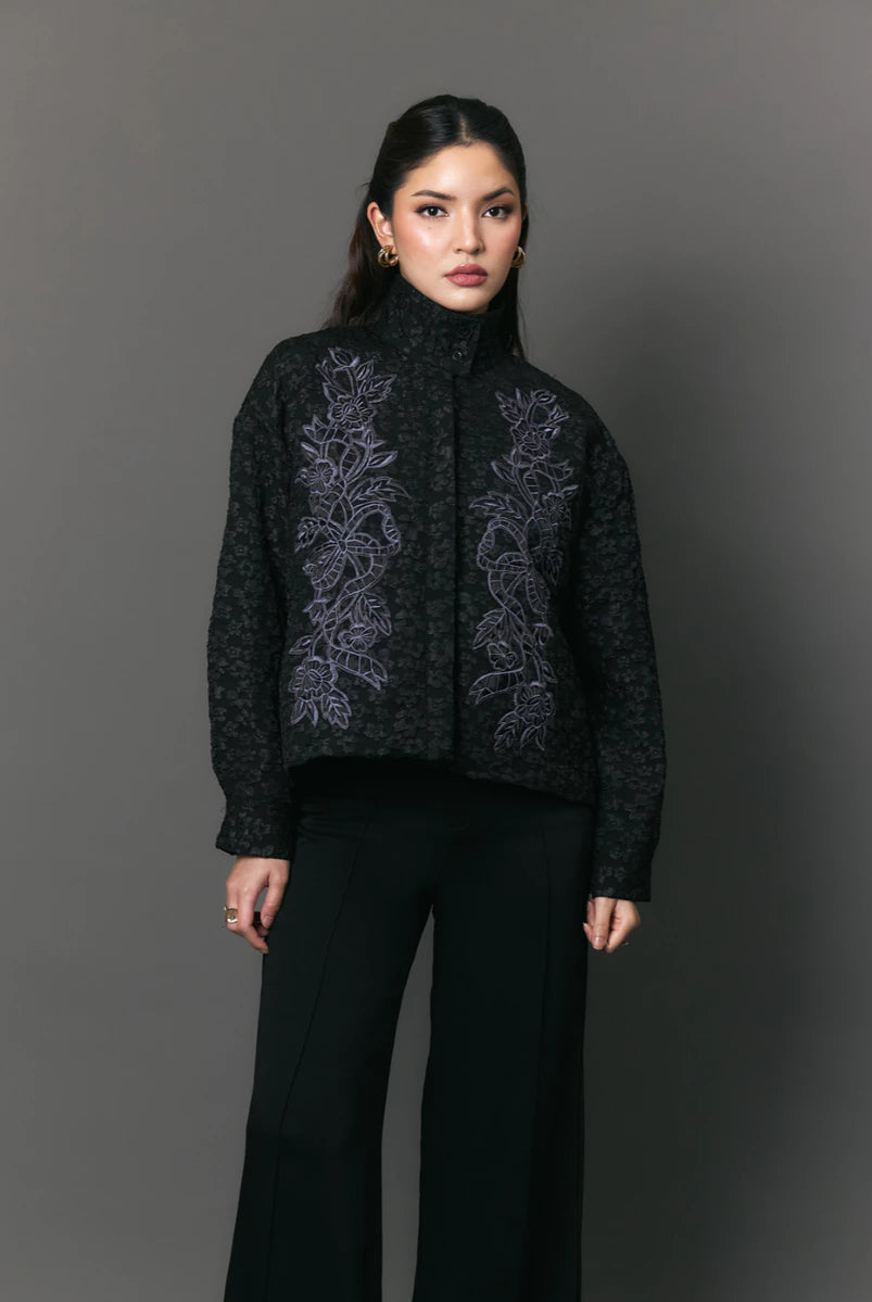 Woman wearing a black jacket with floral embroidery by Studio Tui against a gray background