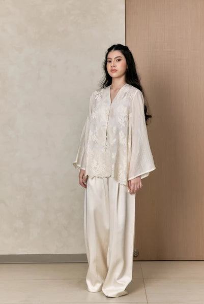 Woman wearing a white shirts with floral details by Studio Tui against a neutral background