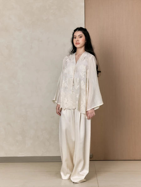 Woman wearing a white shirts with floral details by Studio Tui against a neutral background