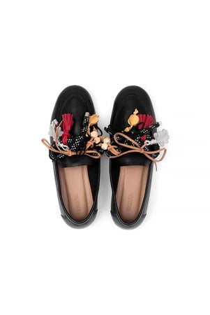 Black loafers flat shoes with colorful tassel decorations by Cajsa on a white background