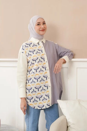 Woman wearing a patterned shirt by Abame in a room with a white wall and couch.
