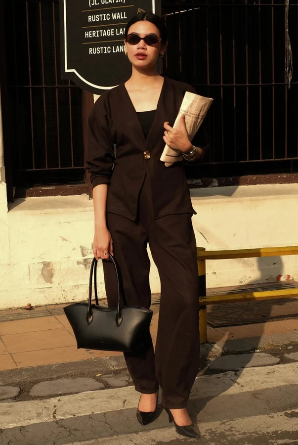 Woman in a black outfit holding a black woman's handbag by Prior against a building background.
Seorang wanita berpakaian hitam memegang tas tangan wanita hitam buatan Prior di depan latar belakang bangunan.