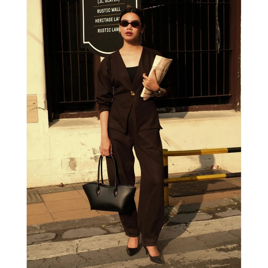Woman in a black outfit holding a black woman's handbag by Prior against a building background.
Seorang wanita berpakaian hitam memegang tas tangan wanita hitam buatan Prior di depan latar belakang bangunan.