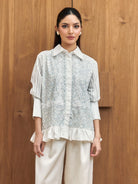 Woman wearing a light-colored blouse with ruffled details by Studio Tui against a wooden background