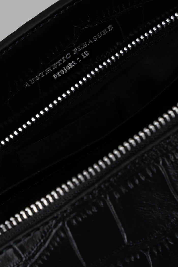 Close-up of a black leather baguette bag by Aesthetic Pleasure with embossed text and zipper