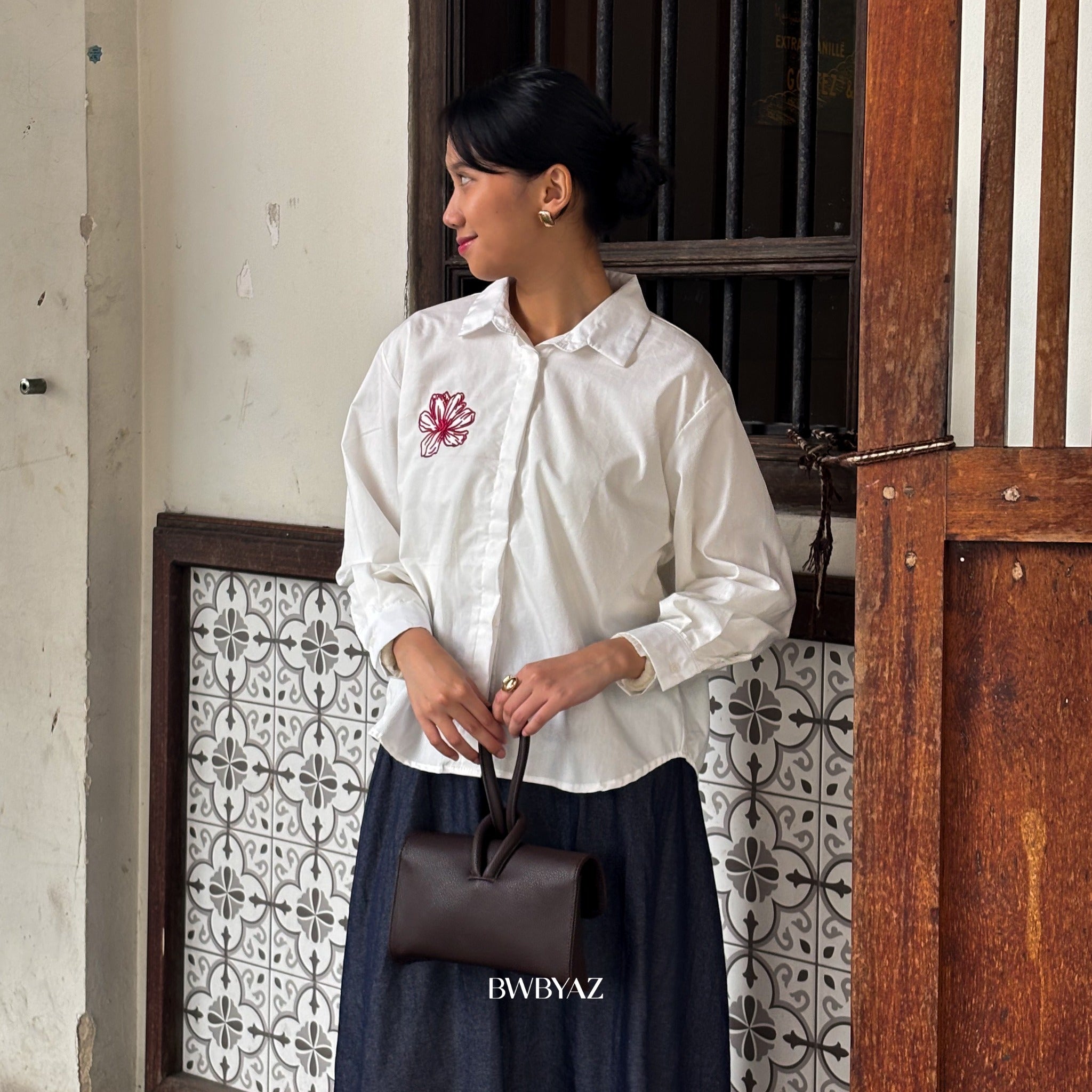A woman wearing a white Adelaine embroidery shirt with a rose design on the chest from BWBYAZ, paired with a dark skirt.