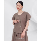 A woman wearing a brown, asymmetrical button-down blouse with short sleeves and a round neckline by Kasyalia.