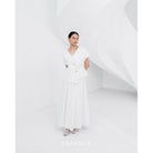 A woman wearing a white, asymmetrical button-down blouse with short sleeves and a round neckline by Kasyalia.