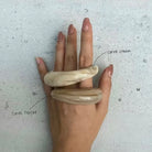 Hand wearing two beige acrylic bangle by Darje on a light gray background
