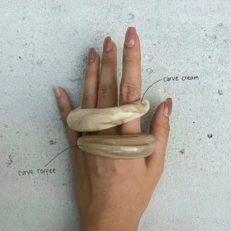 Hand wearing two beige acrylic bangle by Darje on a light gray background