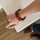 Person wearing a brown acrylic bracelet by Darje on a white surface with a wooden floor.