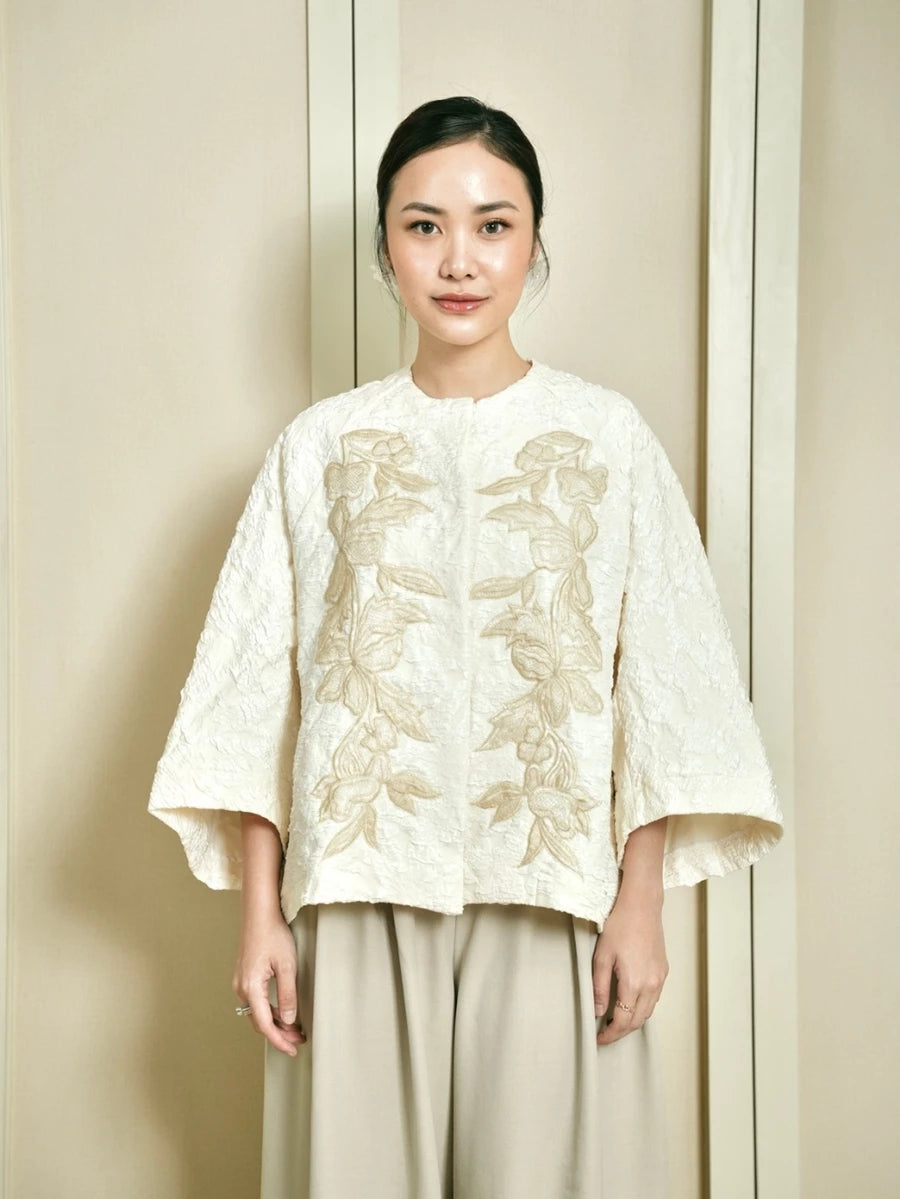 Woman wearing a white outer by Studio Tui with floral patterns against a beige background