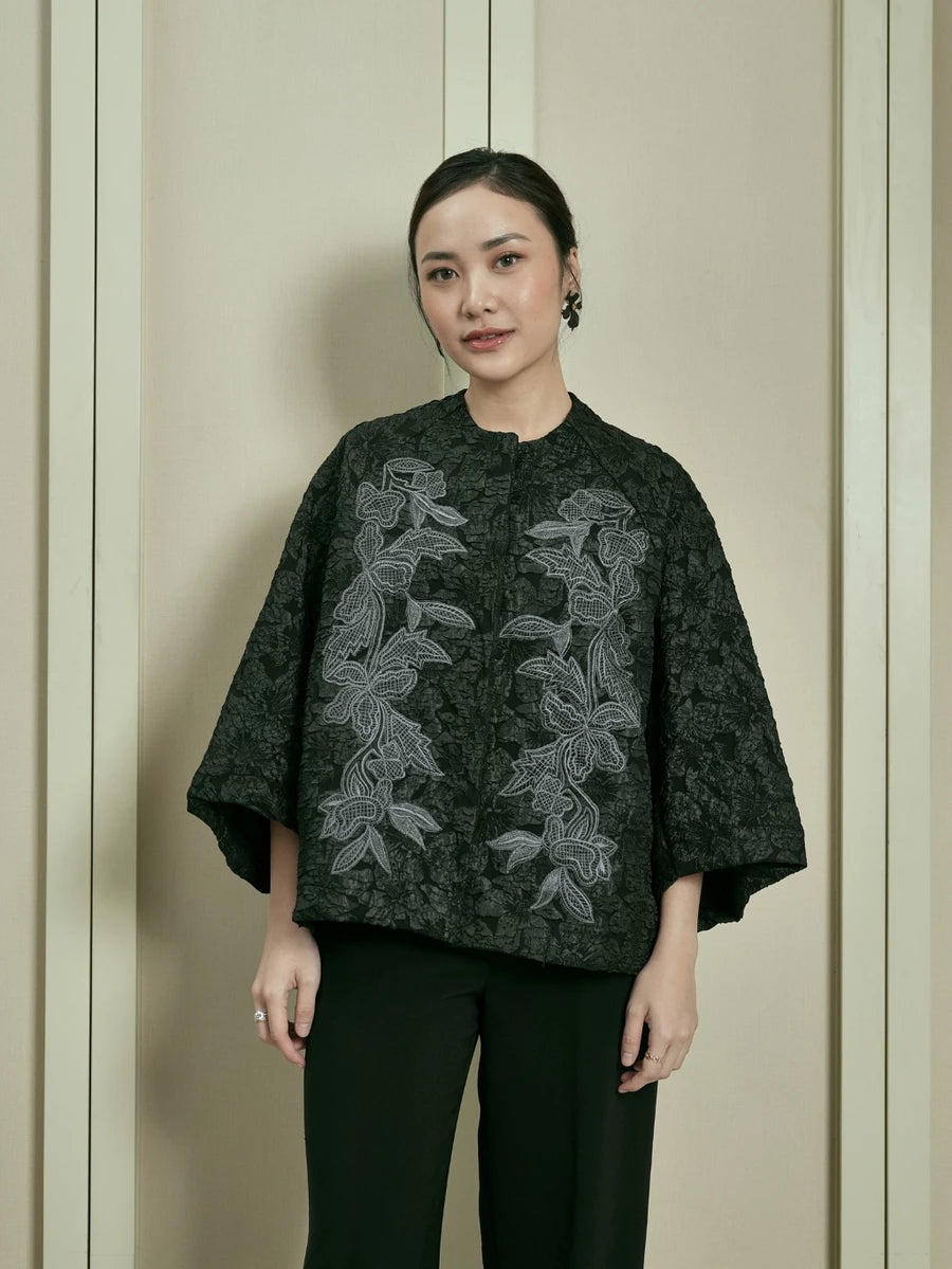 Woman wearing a dark floral embroidered outer by Studio Tui against a neutral background