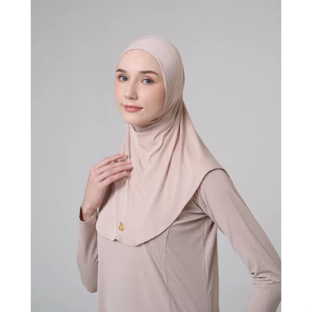 Woman wearing a beige hijab sport by Inanna and dress against a light gray background