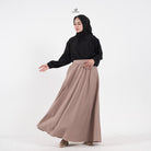 A woman wearing an ash brown linen skirt by Swifter with a wide hemline, flowing fabric, and a lining. She has a zipper at the left side and a pocket at the right side on the skirt.