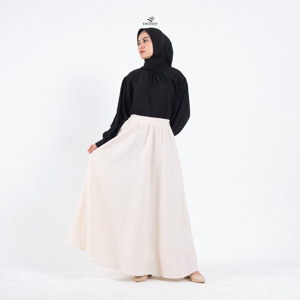 A woman wearing a white linen maxi skirt by Swifter with a wide bottom and a lining. She has a black top and is posing against a white background.