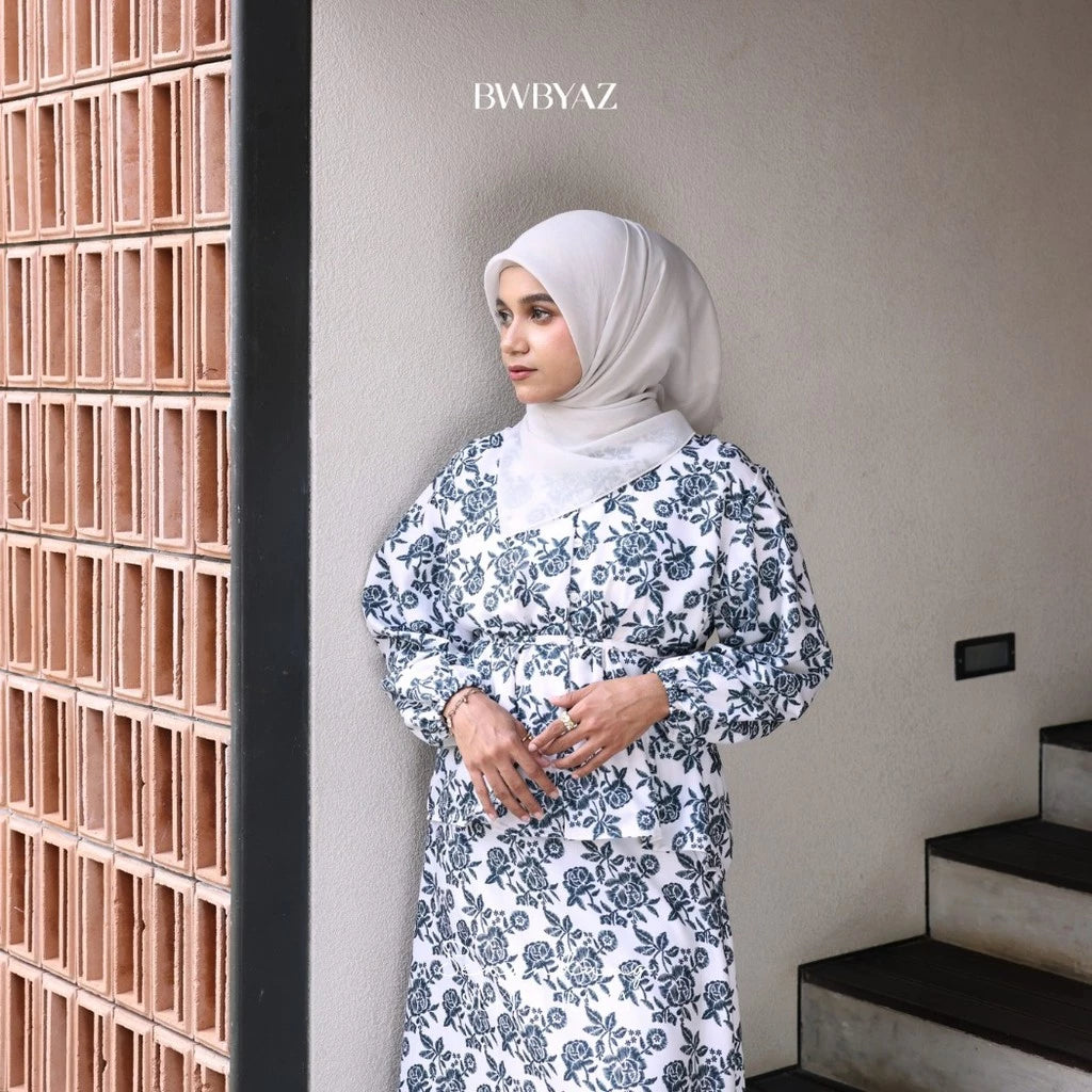 A person wearing a blue Alisha blouse with a floral pattern, featuring a loose fit and front waist tie from BWBYAZ.